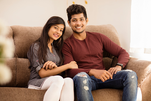 Cute happy young Indian couple relaxing on sofa at home.